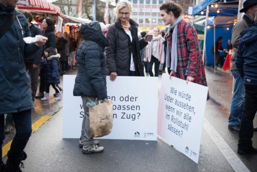 Stadtpräsidentin Barbara Thalmann mit Elisabeth Hildebrand, Inklusionskoordinatorin, auf dem Ustermarkt. Sie tragen beide eine Fragentafel und sind im Gespräch mit einer älteren Frau.