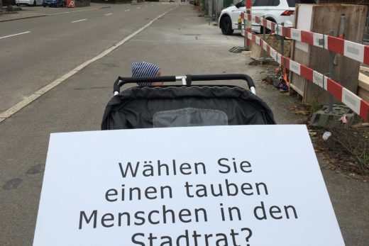 Ein Doppelkinderwagen auf der Strasse. Darauf liegt die Fragentafel: Wählen Sie einen tauben Menschen in der Stadtrat?": "