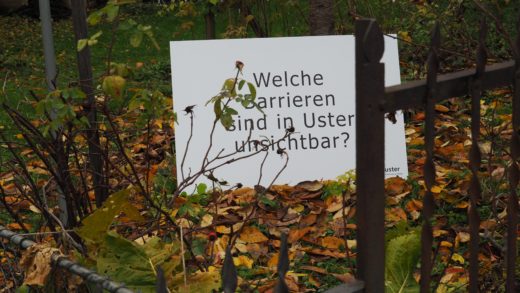 Fragentafel im Garten ausgestellt. Darauf die Frage: Welche Barrieren sind in Uster unsichtbar?