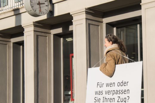 Eine Fragenträgerin mit ihrer Frage am Bahnhof Uster: "Für wen oder was verpassen Sie Ihren Zug?", steht auf der Tafel.