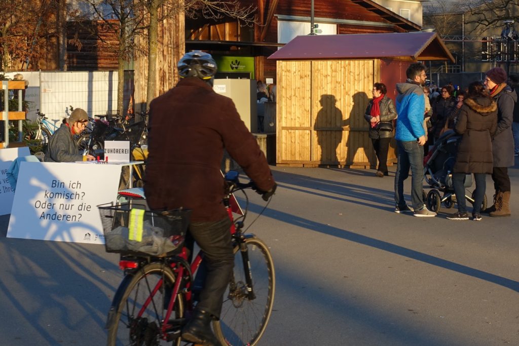 Die Zuhörerei steht vor der Landihalle. Ein Maann fährt mit dem Velo dran vorbei.