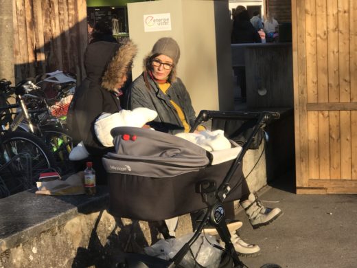 Zwei Frauen unterhalten sich. Sie sitzen auf einer Mauer. Die eine FRau hat ein Babay im Arm.