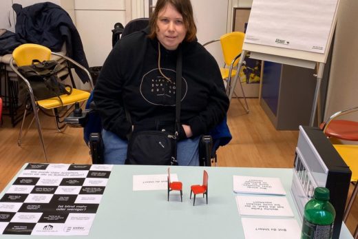 Junge FRau im Rollstuhl sitzt am Tisch der Zuhörerei im Produktwerk des Werkheims.