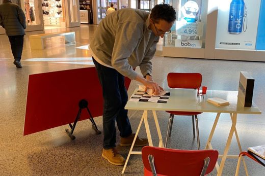 Linus Hut klebt ein Plakat auf den Tisch der Zuhörerei