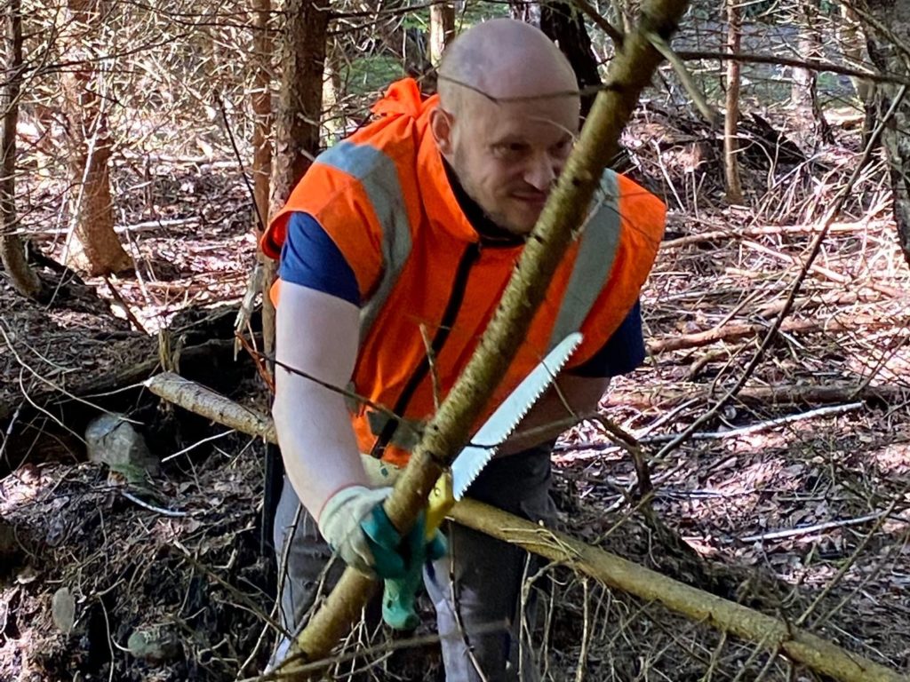 Ein Bewohner des Werkheims mit Sicherheitsweste arbeitet im Wald