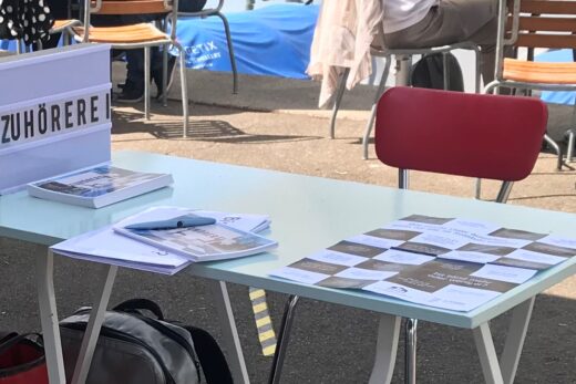 Der Tisch und ein Stuhl der Zuhörerei. Auf dem Tisch liegt ein Pakat mit verschiedenen Fragen zum Thema Stadt für alle