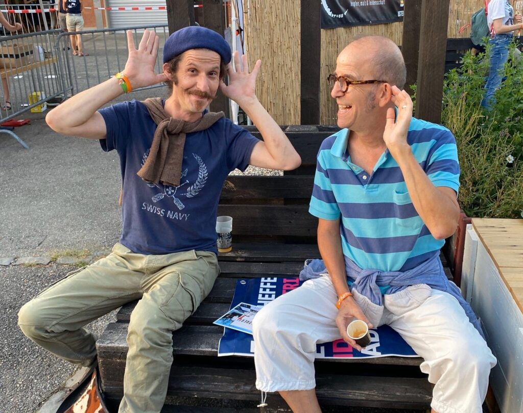 Rolf und Reneé sitzen zusammen auf einem Holzpalett am H"U in Uster. Rolf macht den Kaspar.