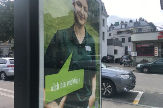 Ein Plakat im öffentlichen Raum bei Bahnhof. Es zeigt eine junge Frau in grünem Pullover. Sie lächelt. Auf dem Plakat ist zu lesen: Ich bin wichtig.